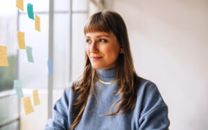 Thoughtful young businesswoman standing next to a glass wall