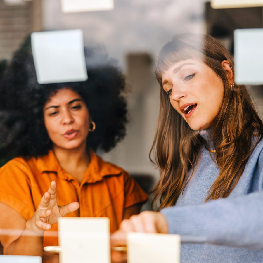 Two creative businesswomen brainstorming using adhesive notes. Businesswomen discussing their business ideas during a meeting. Young female entrepreneurs working as a team in a modern office.